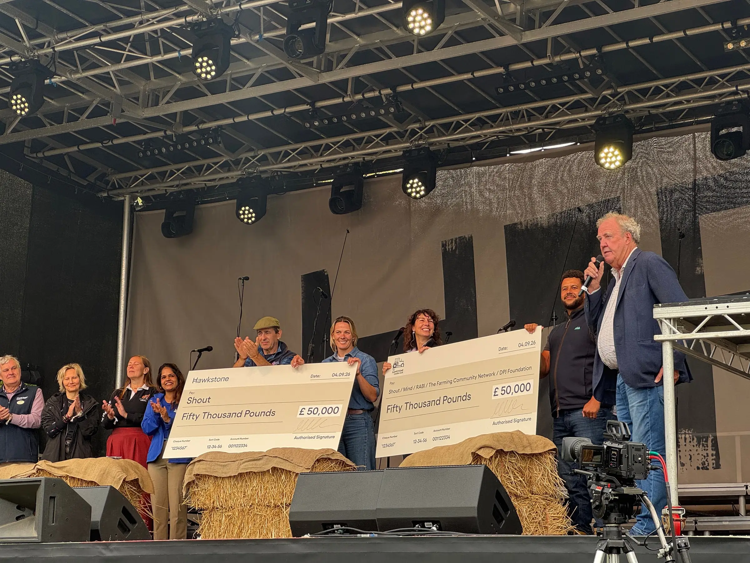 Jeremy Clarkson and the choir presenting charity donation cheques on stage