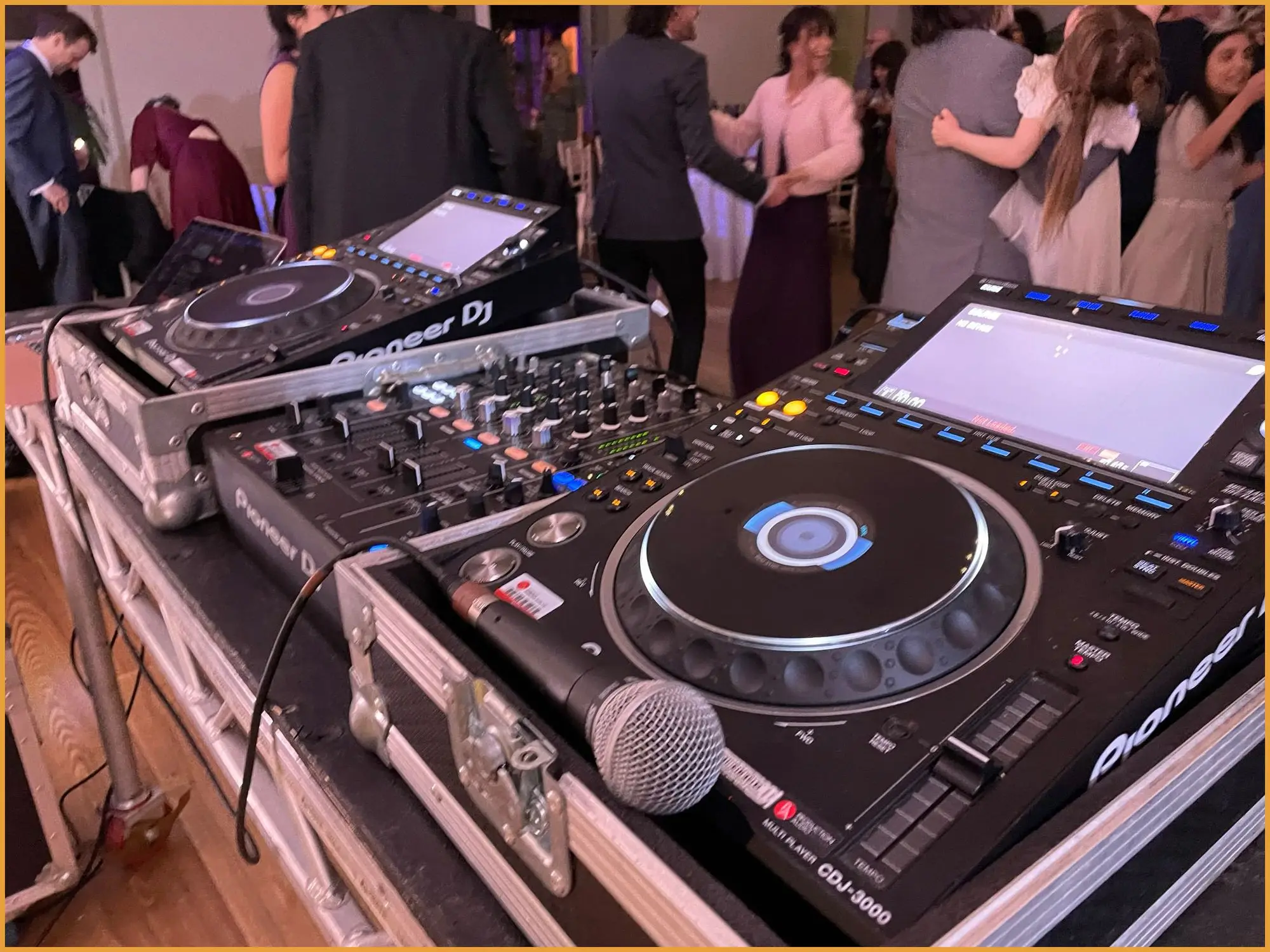DJ with arms raised behind the decks in front of a light curtain