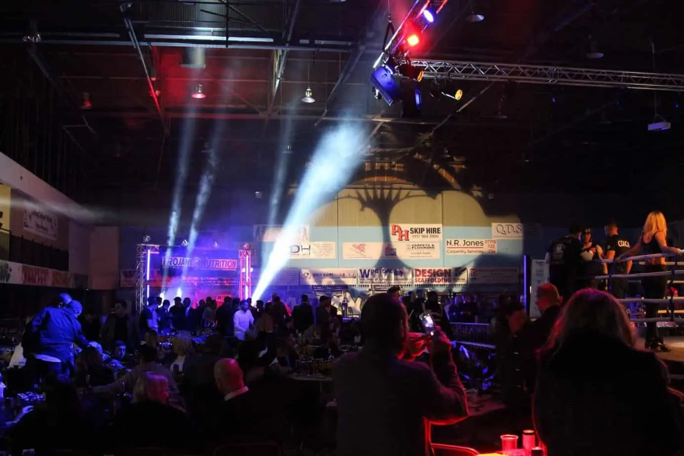 Boxing night in a large hall with beams of light cutting through haze above the audience