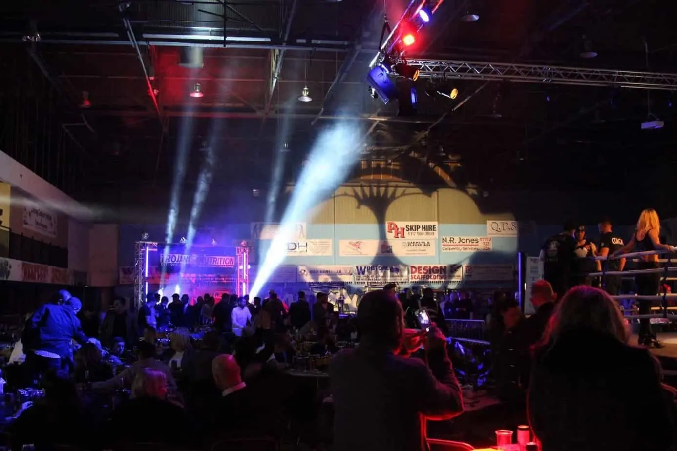 Boxing night in a large hall with beams of light cutting through haze above the audience