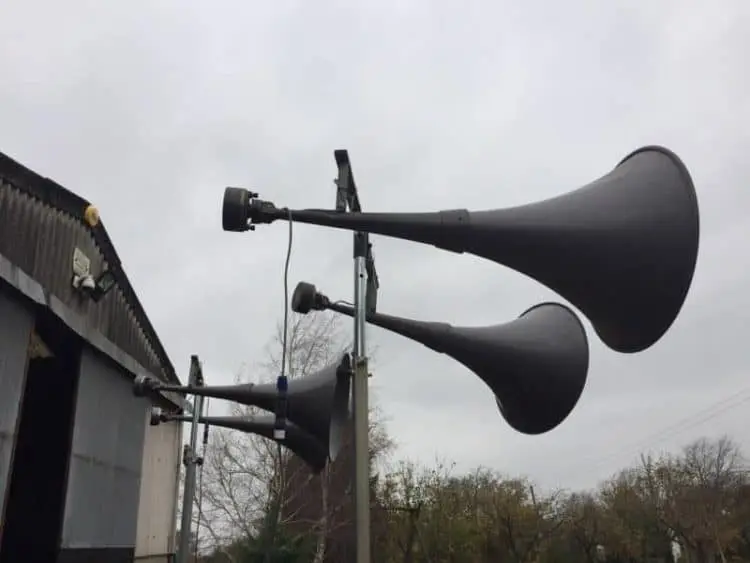 Two horn loudspeakers mounted on a pole against a grey sky