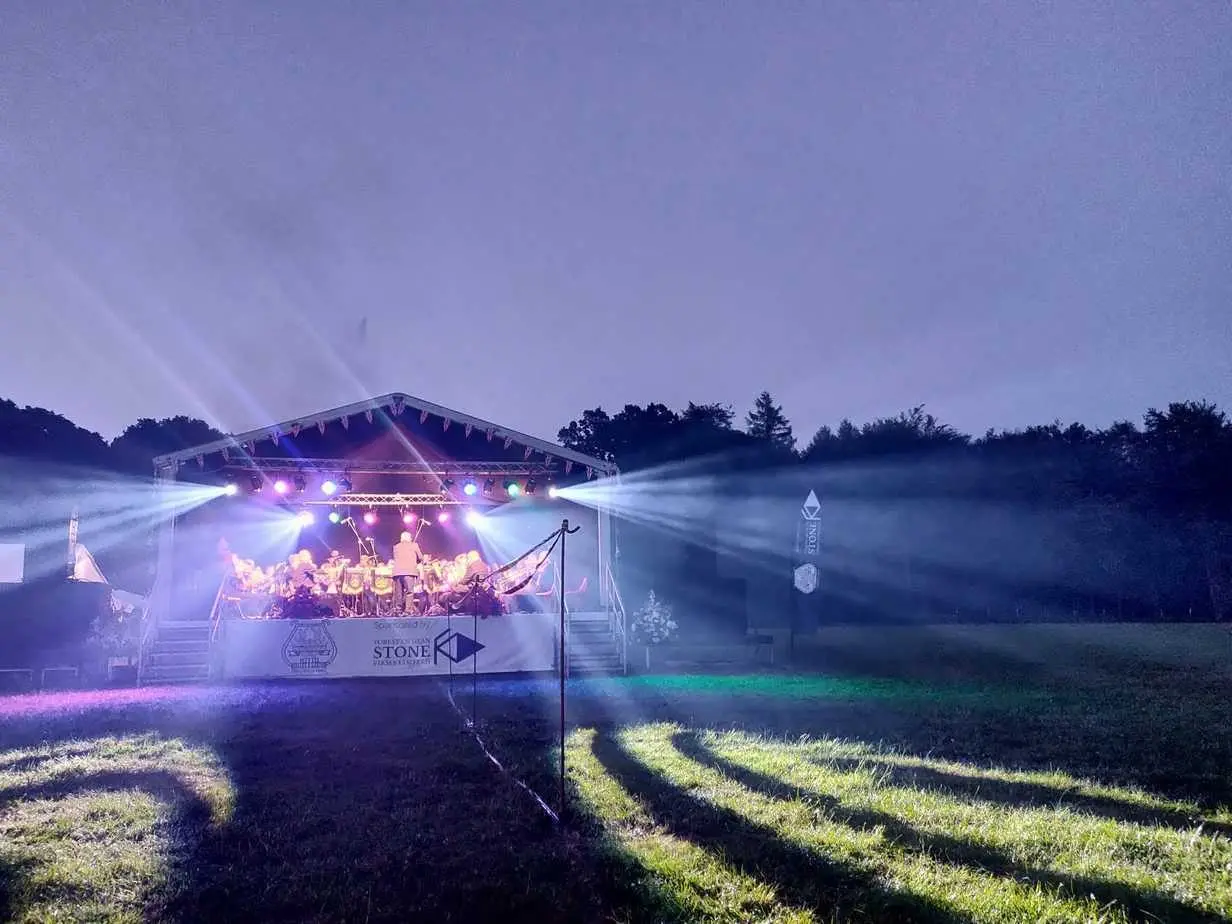 Outdoor stage lit at dusk with beams of light across a field