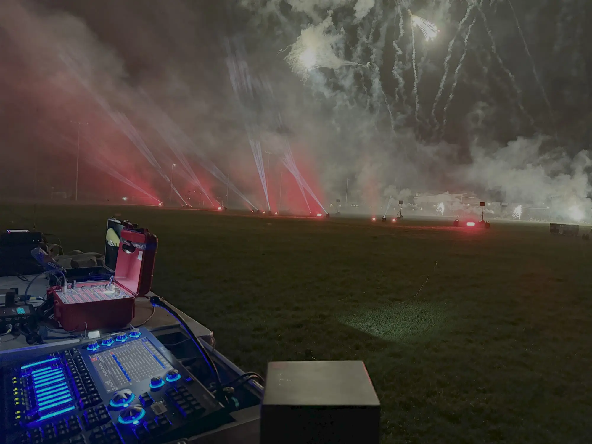 Beams of light and fireworks over a dark field, with a lighting desk in the foreground