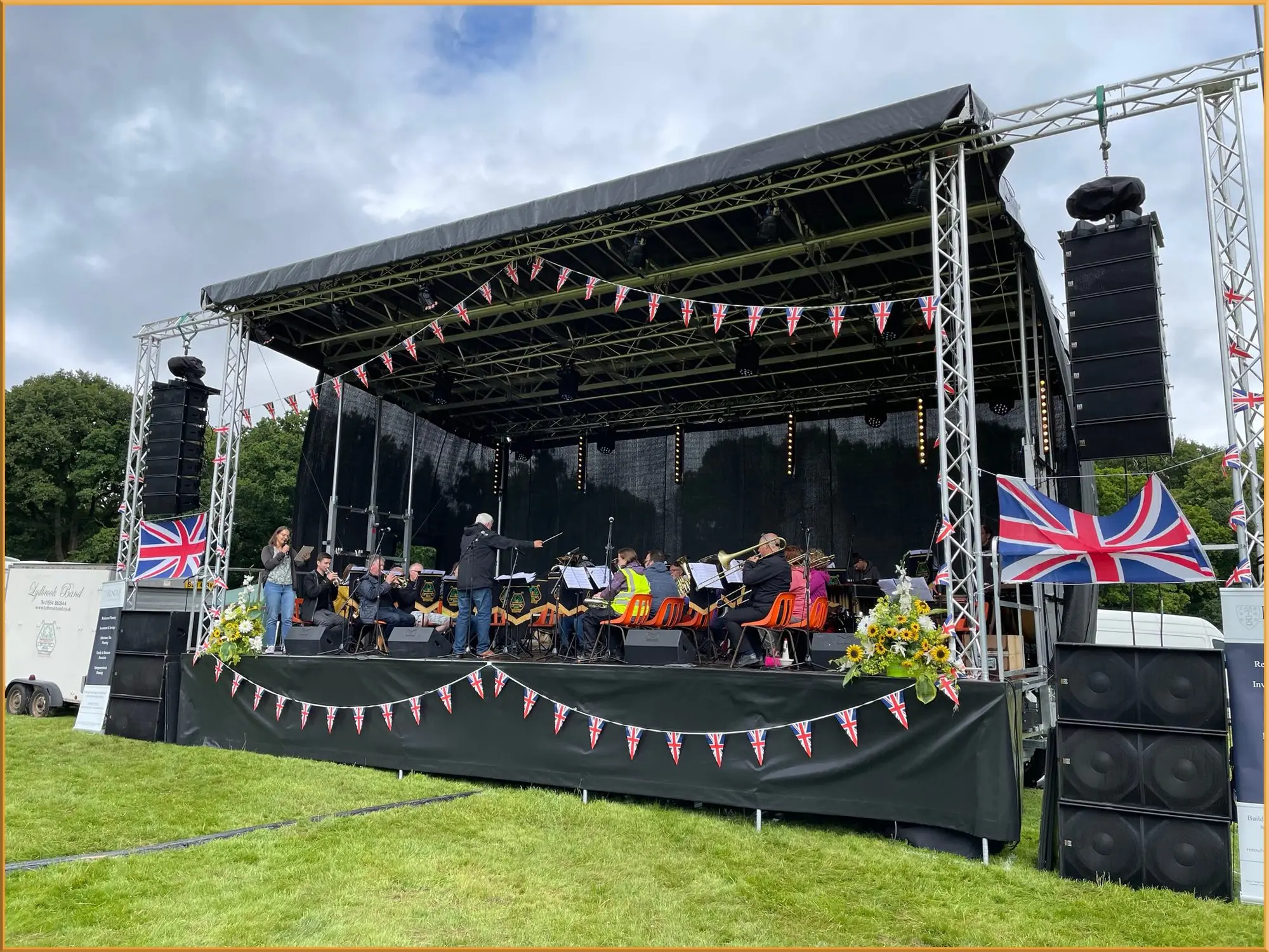 Outdoor stage decorated with bunting and Union Jack flags, with an orchestra performing