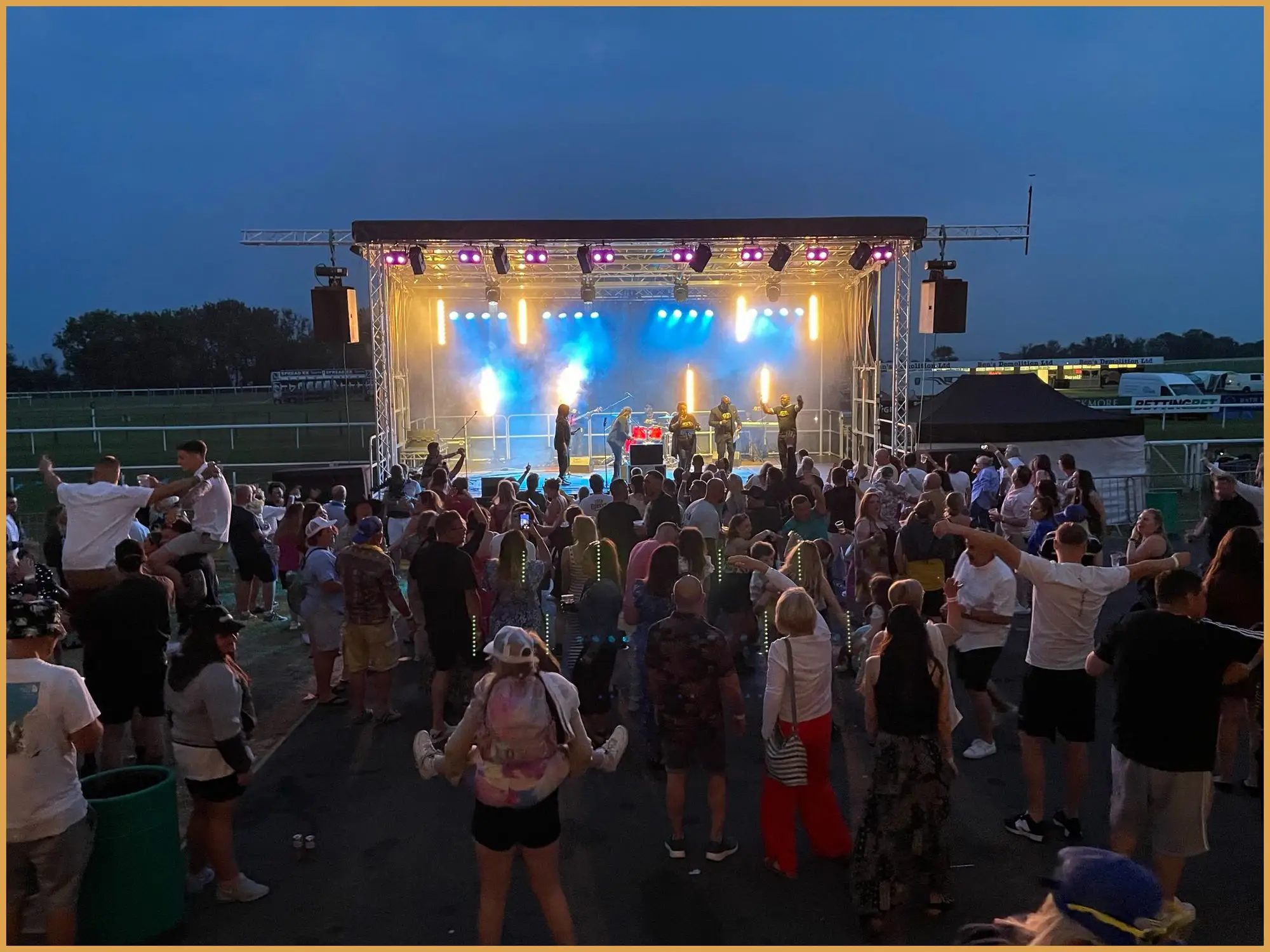 Crowd in front of a lit festival stage at dusk