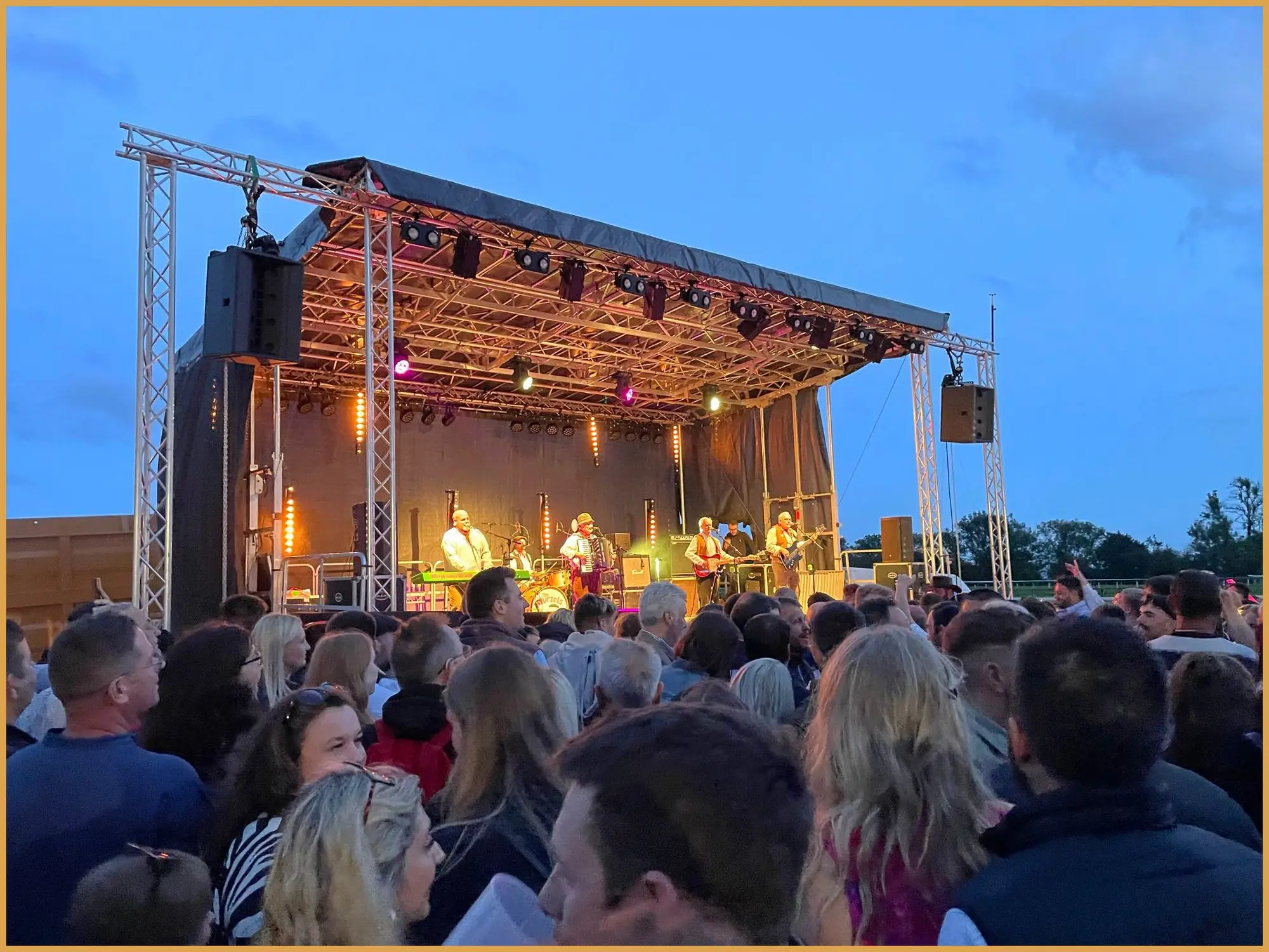 Festival stage at dusk with the crowd gathered in front