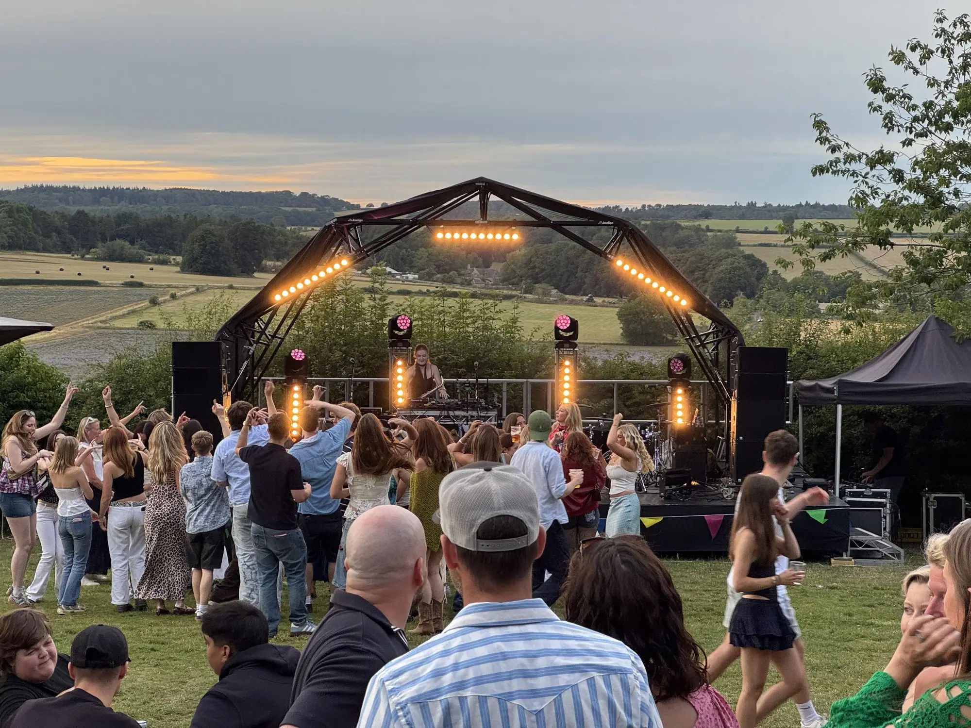 Konligo Fastival stage roof at dusk with a crowd dancing and Cotswold hills behind