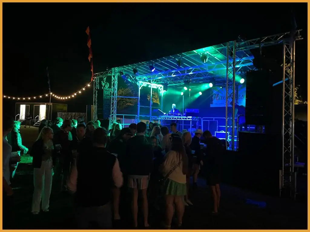 Outdoor festival stage lit in blue and purple with guests in front at night