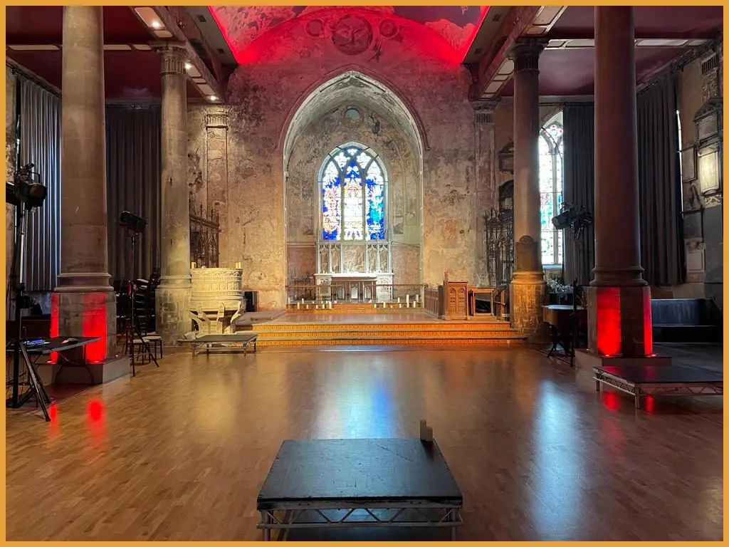 The Mount Without in Bristol lit in red with a stage platform in front of the stained glass window