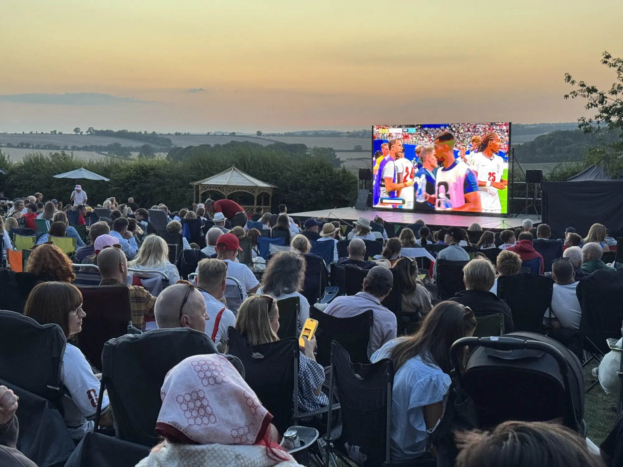 Large outdoor LED screen showing World Cup football to a crowd at sunset